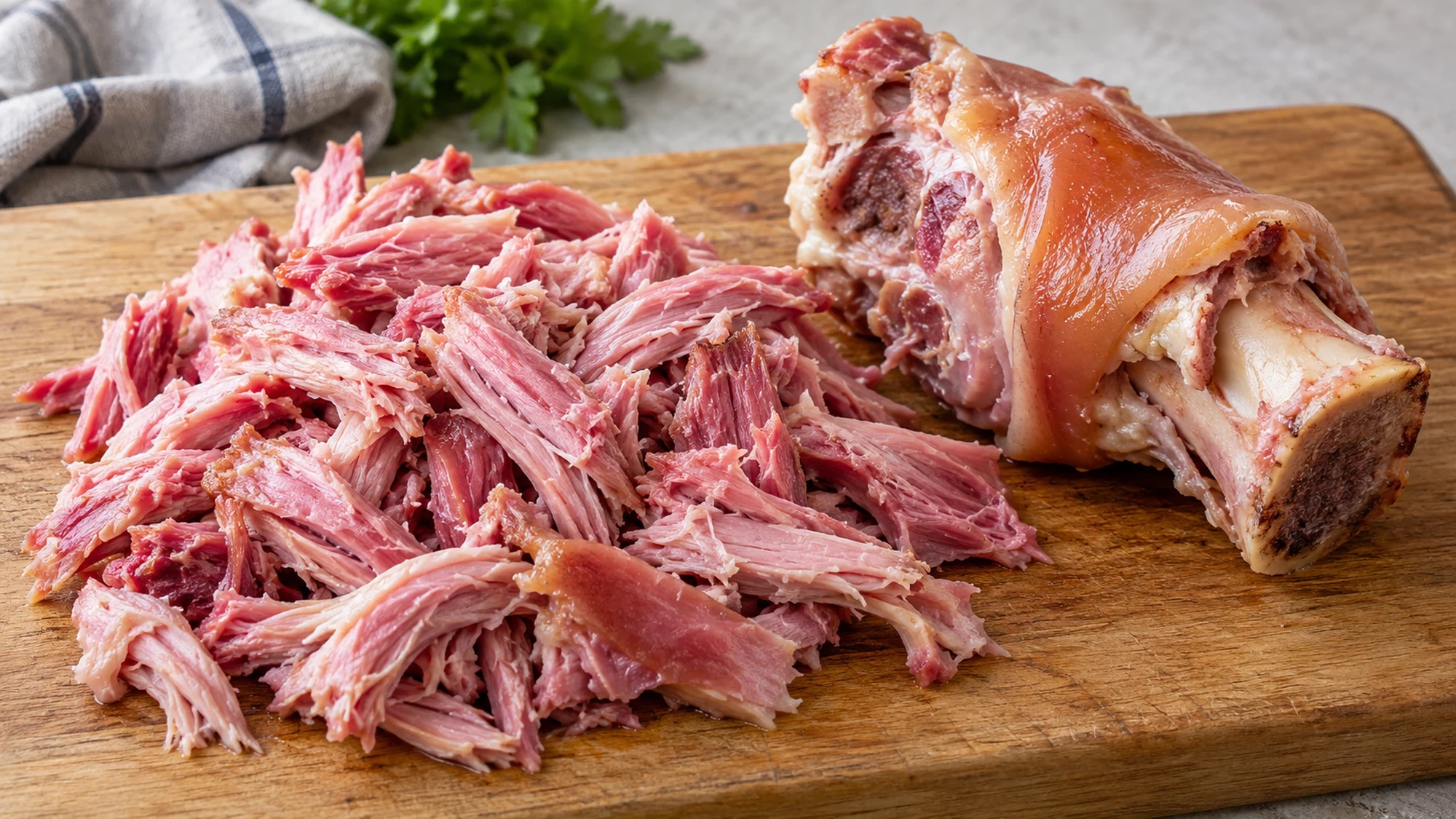 Shredded pink cooked gammon hock meat beside the remaining bone and rind