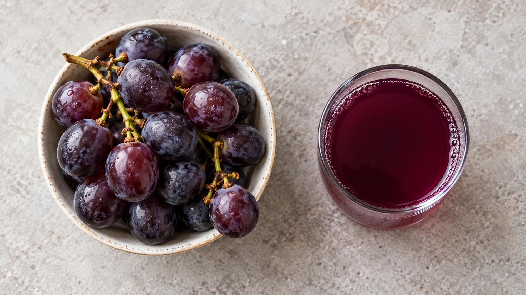 Overhead view of whole grapes in a bowl beside a small glass of grape juice