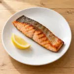 Grilled skin-on salmon fillet with a lemon wedge