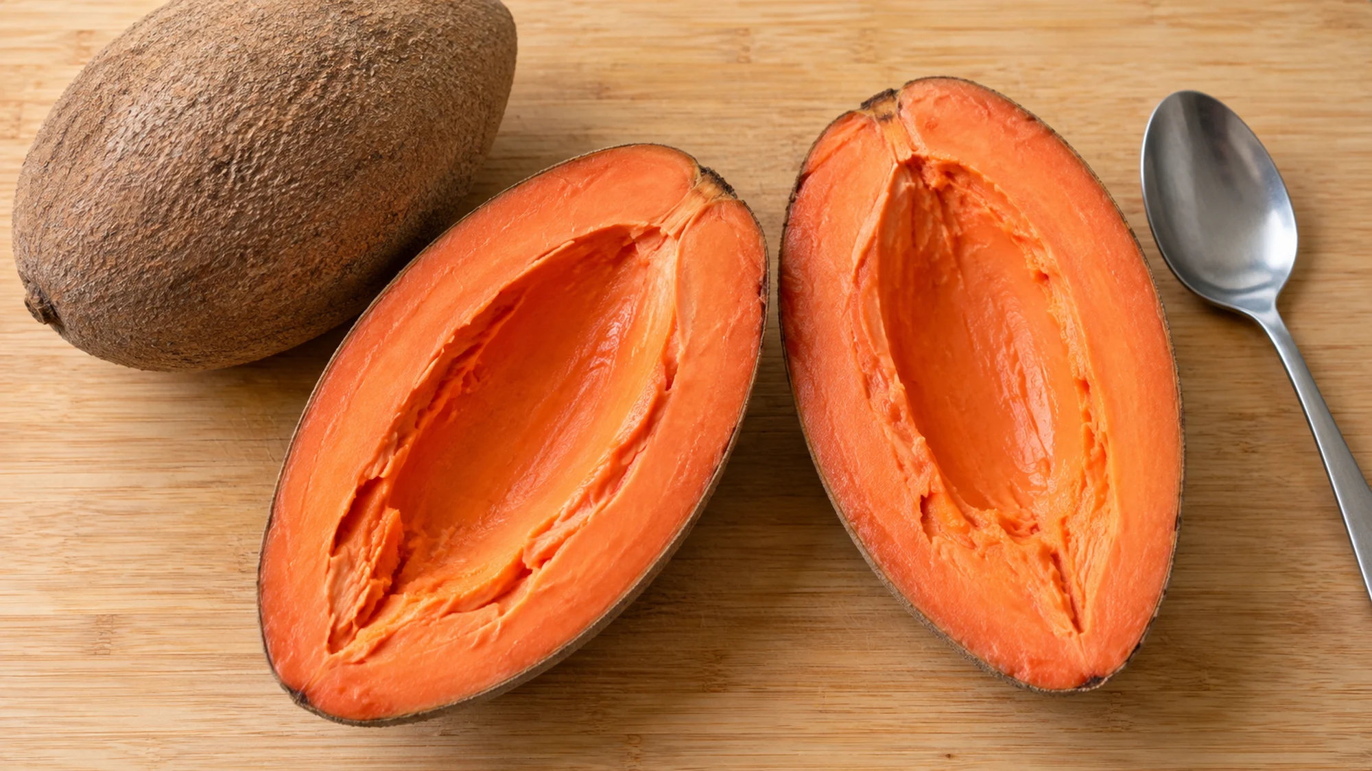 Mamey halves with the seeds removed on a wooden board beside a spoon