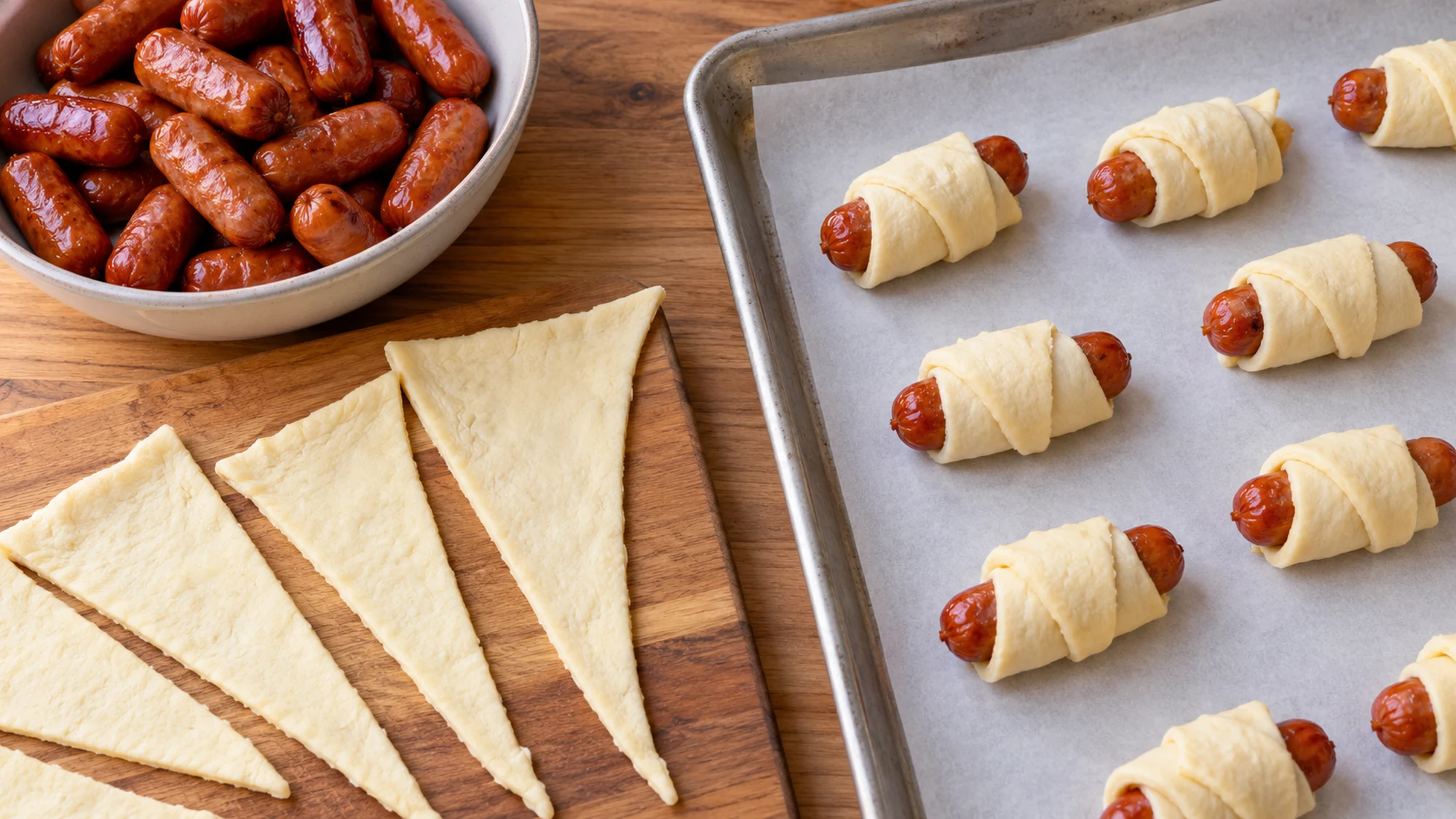 Cocktail sausages rolled in narrow crescent dough triangles on parchment