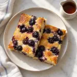 Blueberry sheet-pan pancakes on a ceramic plate beside syrup