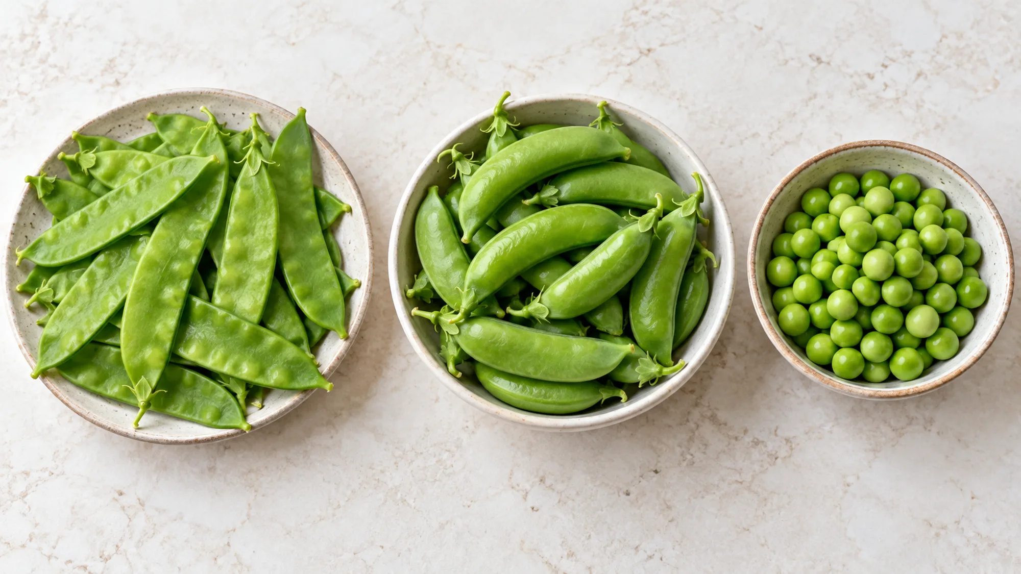 Snow peas beside rounded snap peas and shelled green peas