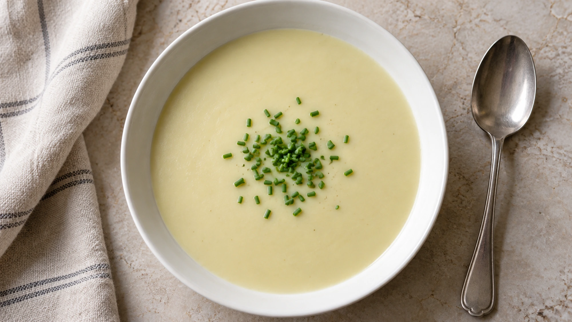 A shallow bowl of chilled vichyssoise served with a spoon