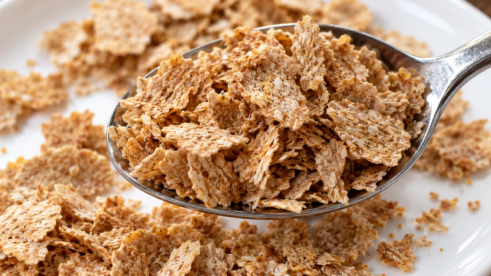 Papery brown wheat bran flakes on a spoon over a white plate