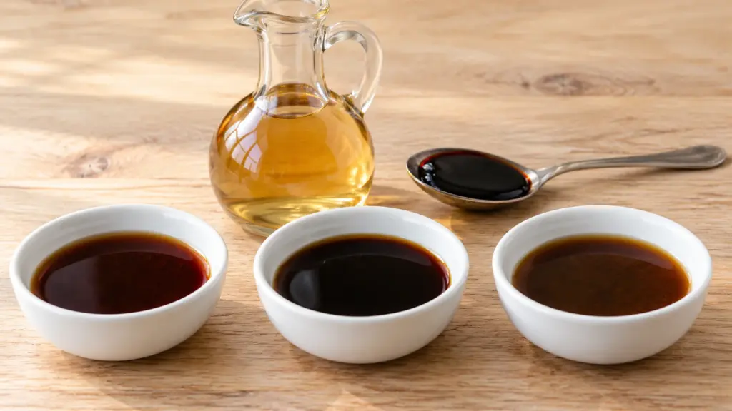 Three bowls of dark seasoning sauces beside cider vinegar and a spoon of molasses